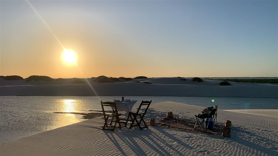Pôr do sol nas dunas com mesa preparada à beira da lagoa