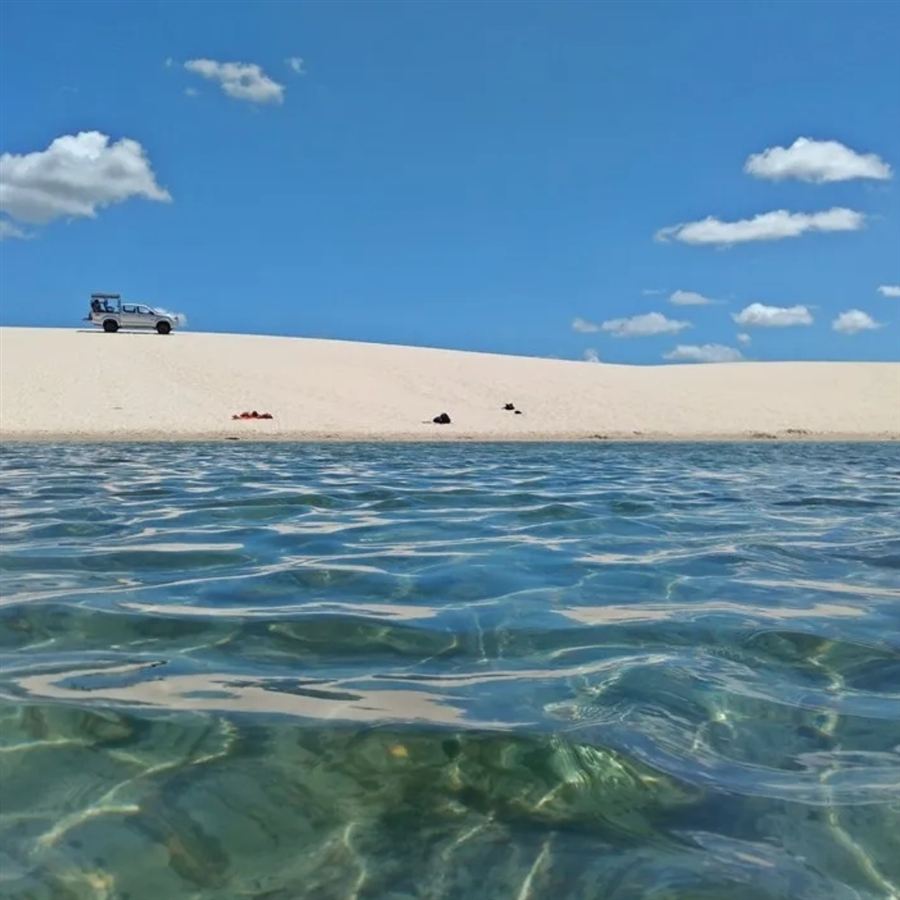 Veículo 4x4 sobre duna com lagoa de água cristalina